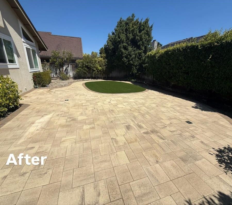 The same backyard after pool removal, finished as a light paver patio with a circular turf inset
