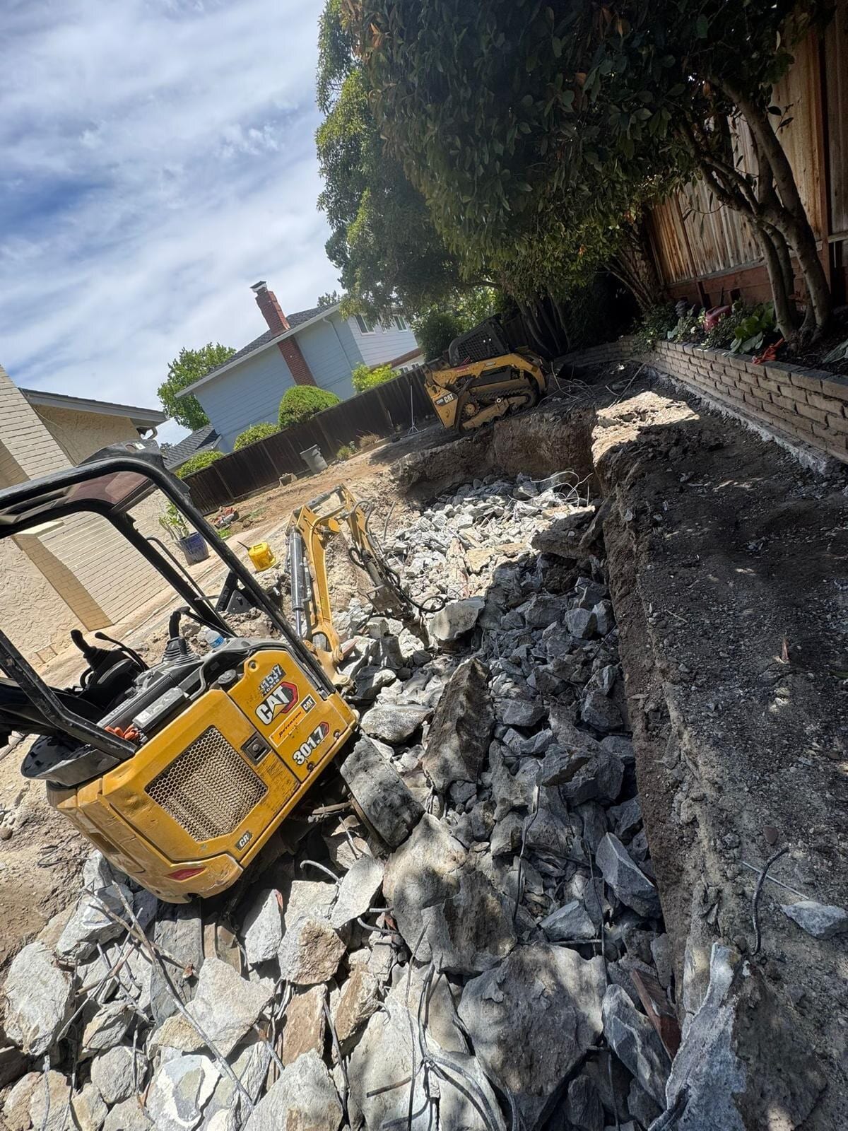 Mini excavator breaking a swimming pool shell into rubble in a Bay Area backyard