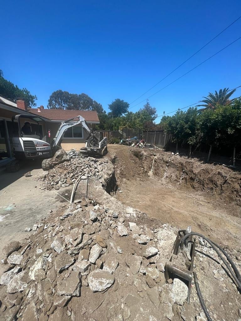 Broken pool concrete stockpiled beside a skid steer during a Bay Area pool demolition