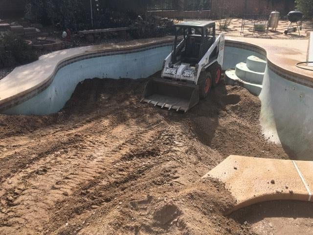 Skid steer placing engineered backfill inside an empty swimming pool shell during a Royal Demolition backfill and compaction job