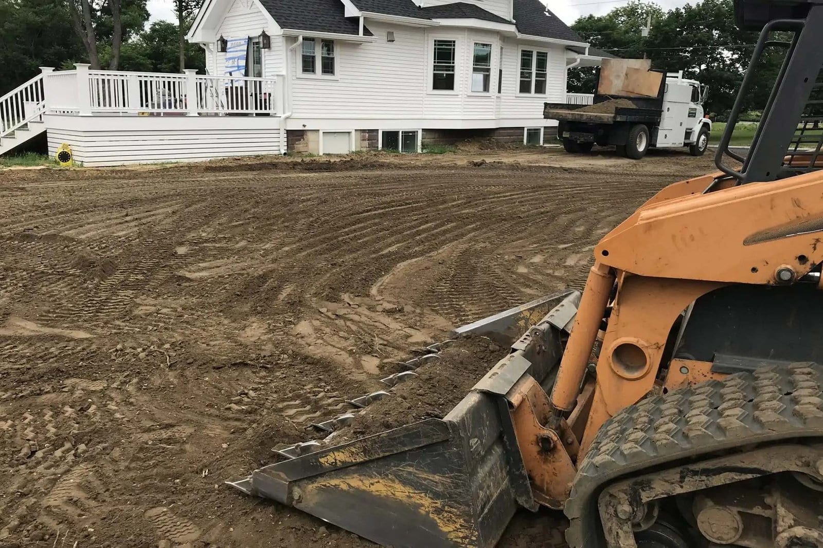 Track loader grading a residential lot flat with a dump truck waiting to haul the spoil away